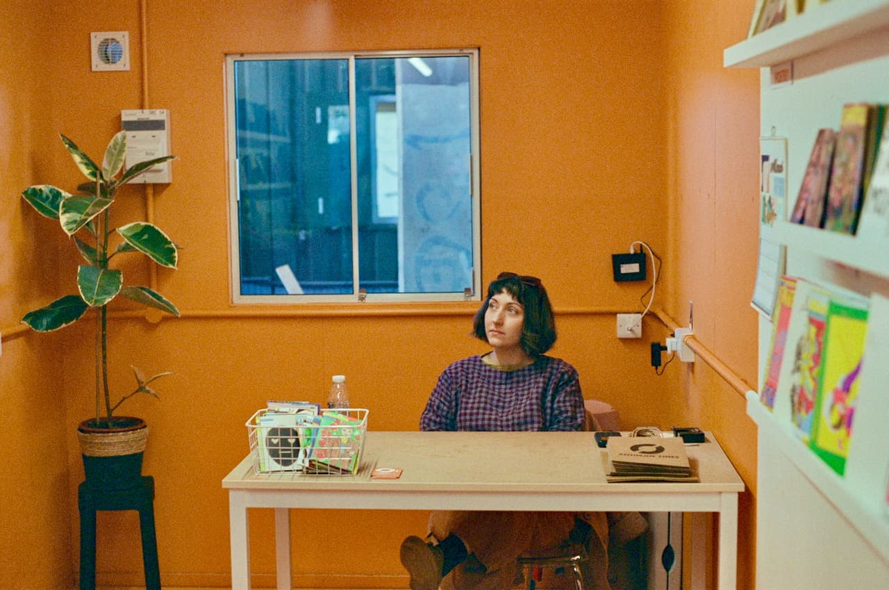 Woman seated at a desk in an orange-walled zine shop