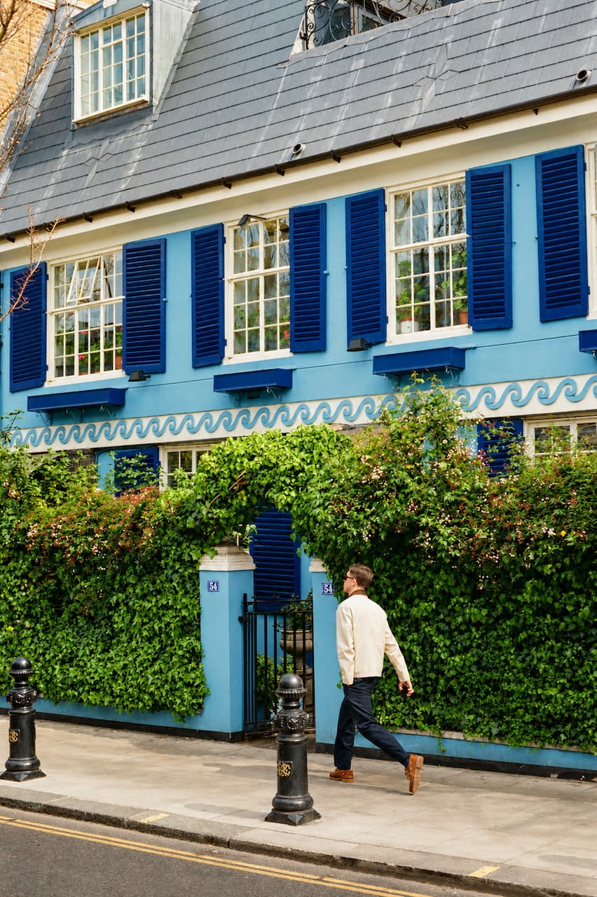Man walking past a blue Victorian house with shutters