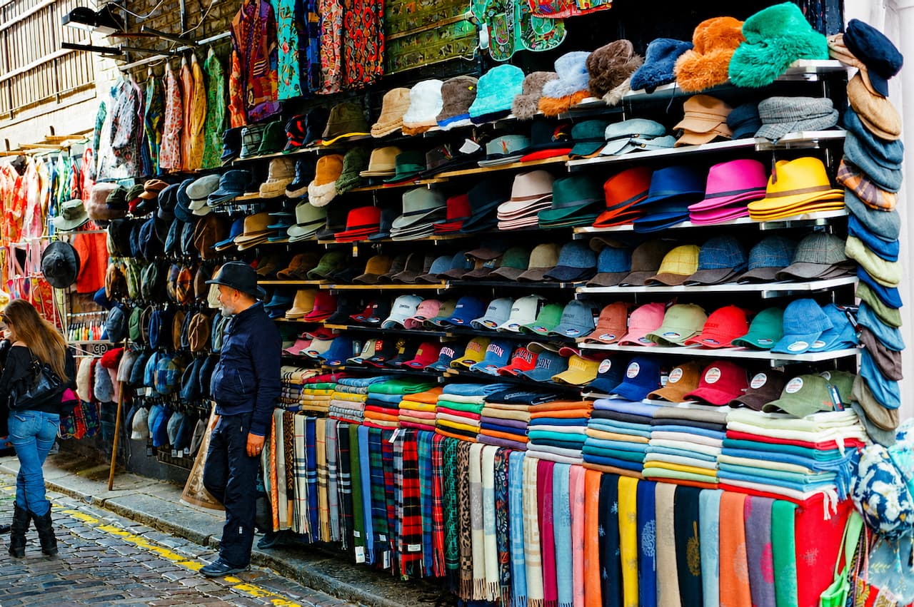 Hat stall at a London market with rows of hats and folded scarves