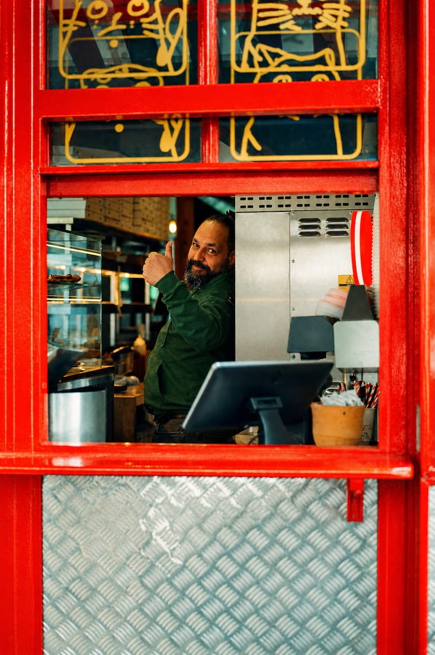 Man behind a counter giving a thumbs up framed by a red window