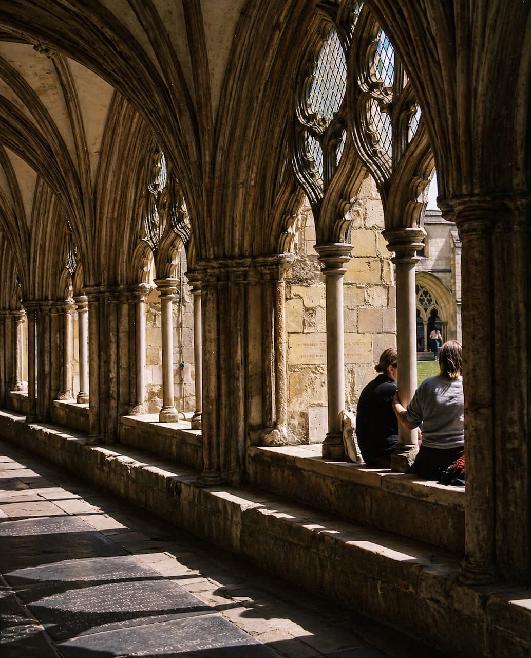 Two figures resting in a sunlit cathedral cloister