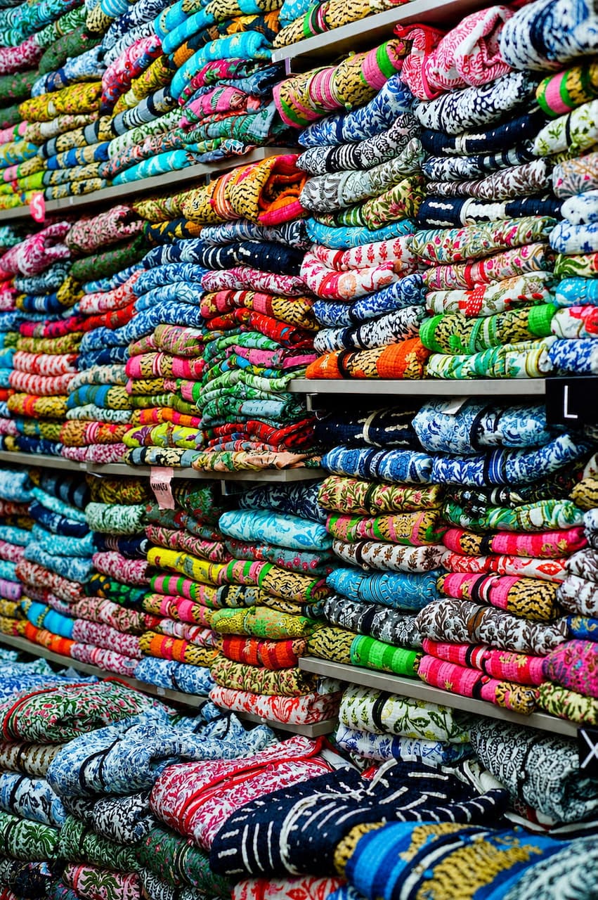 Stacks of patterned fabrics piled on market shelves