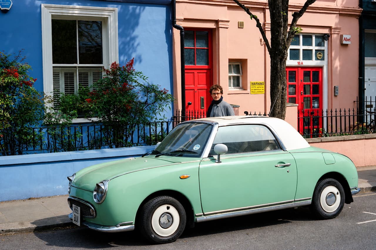 Mint green vintage car parked between blue and pink houses