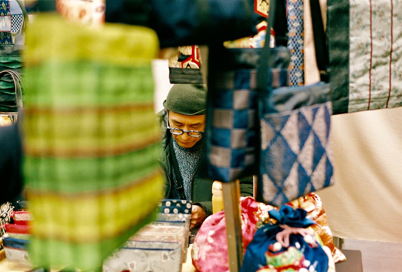 Stallholder among hanging scarves and bags at a market