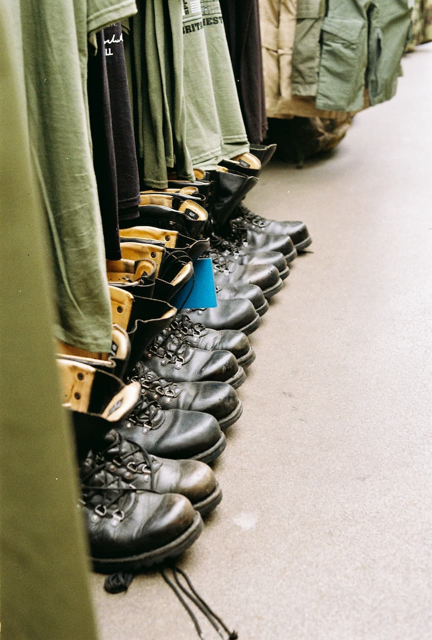 Row of black combat boots beneath army surplus clothing