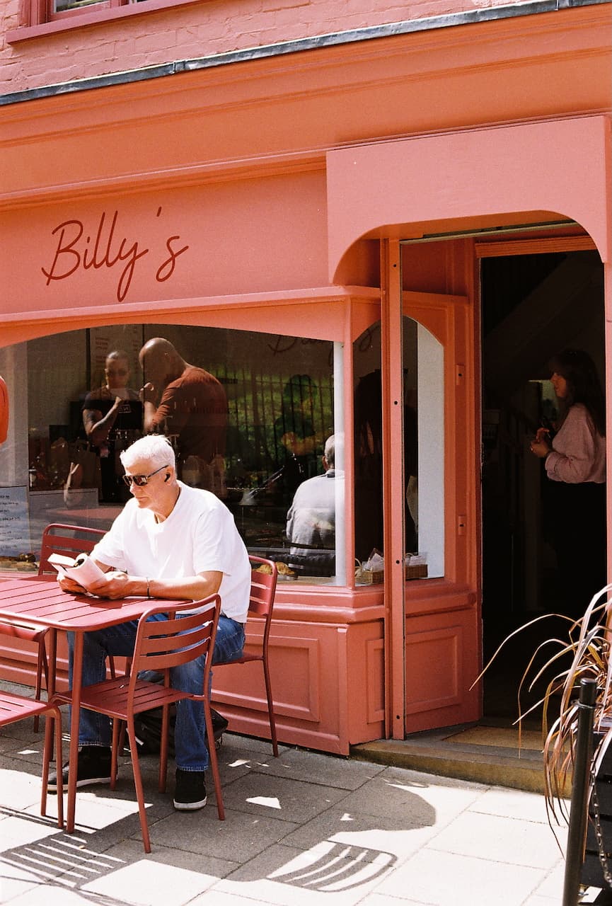 Man reading a book outside Billy's, a pink-fronted café